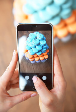 Female hands making photo of varicolored macaroons with mobile phone