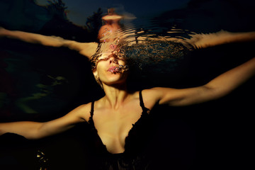 Fototapeta na wymiar girl in a black dress under water blowing bubbles