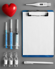 Doctor table with injections, thermometer, clipboard, pen and red heart, top view