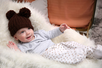 Adorable baby in brown knitted hat in luggage bag in the room, close up