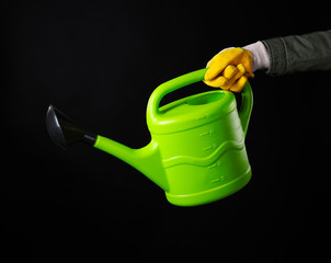 Hand holding green plastic watering can on black background