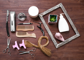 Frame with strand of hair, barber tools, equipment and cosmetics on wooden background