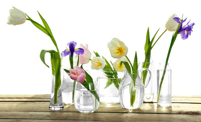 White, pink tulips and purple iris in glass vases with water on wooden table, isolated on white