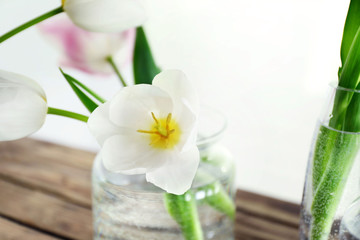 White tulip in glass vase with water on wooden table, close up