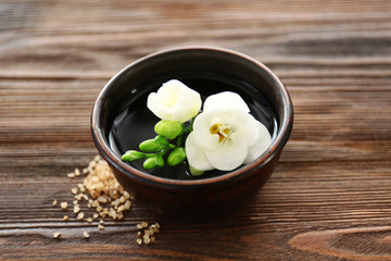 Beautiful flower in the bowl with water and sea salt on wooden background