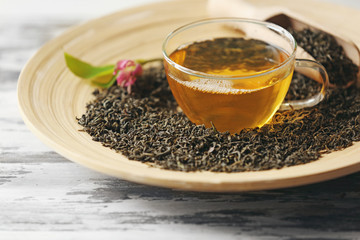 Glass cup of green tea with leaves on wooden plate closeup