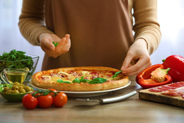 Woman decorating fresh baked pizza with basil, close up