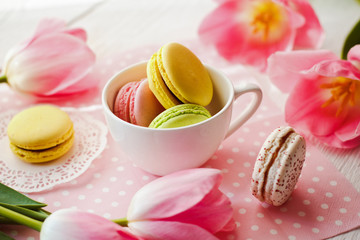 A beautiful flowers pink tulips with colorful macaroons laid in cup on white wooden background with pink Lacy napkin