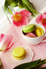 A beautiful flowers pink tulips with colorful macaroons laid in cup on white wooden background with pink Lacy napkin