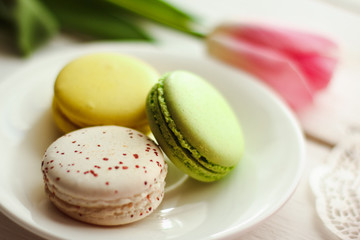 A beautiful flowers pink tulips with colorful macaroons laid on a white platter on white wooden background