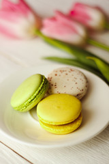 A beautiful flowers pink tulips with colorful macaroons laid on a white platter on white wooden background