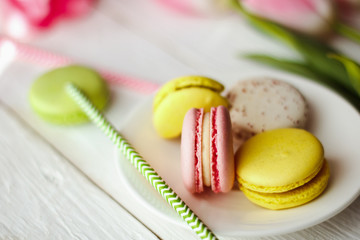A beautiful flowers pink tulips with colorful macaroons laid on a white platter on white wooden background