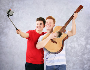 Two teenager boys with guitar using stick for photo by their self on grey background