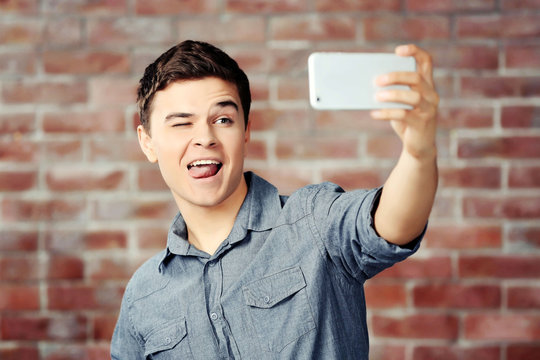 Young handsome boy making photo by his self with mobile phone on brick wall background