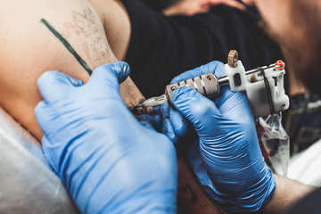 master tattooist does the tattoo in gloves on the hand of the man