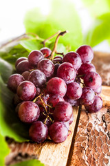 Red grapes branch with green leaves on old wooden board selective focus in studio