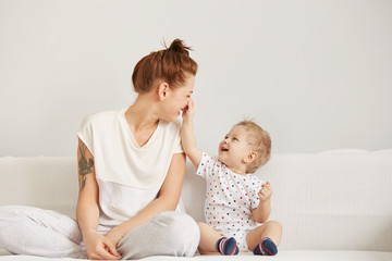 Young mother with her one years old little son dressed in pajamas are relaxing and playing in the...