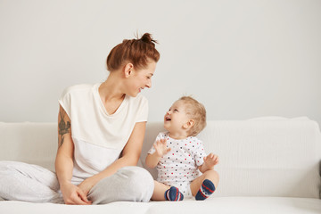 Young mother with her one years old little son dressed in pajamas are relaxing and playing in the...