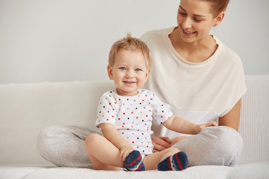Young mother with her one years old little son dressed in pajamas are relaxing and playing in the bedroom at the weekend together, lazy morning, warm and cozy scene. Selective focus.
