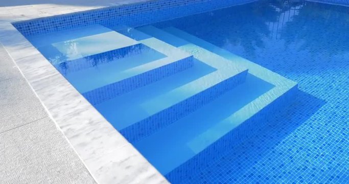 Underwater stairs in outdoor blue tiled swimming pool with clear  water. Spa and resort