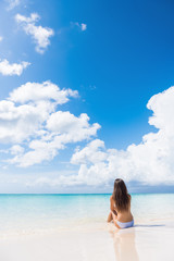 Beach woman enjoying serene luxury vacation relaxing under the sun sitting in water looking at perfect turquoise ocean at tropical getaway paradise. Girl from the back sunbathing.