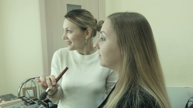 female makeup artist applying makeup on a female client, and telling to the customer as she applying cosmetics