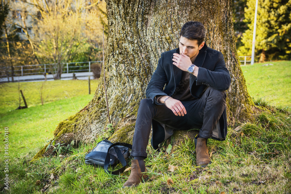 Wall mural Handsome young man leaning against tree