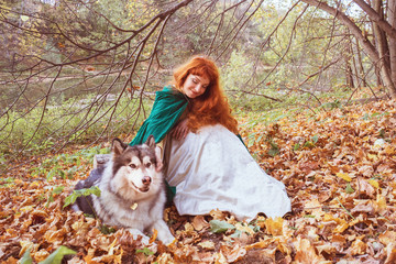 Naklejka na ściany i meble A fairytale fantasy. Red-headed woman in autumn forest. She dressed in renaissance costume. With dog