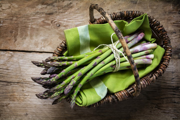 fresh green asparagus in a basket on a rustic wooden table, view from above