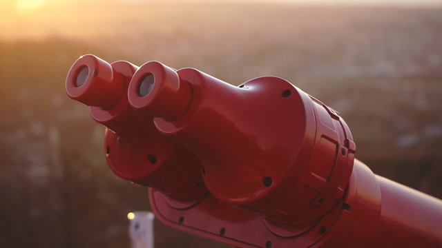 Tourist looking at city through coin-operated binoculars at sunset, closeup back shot