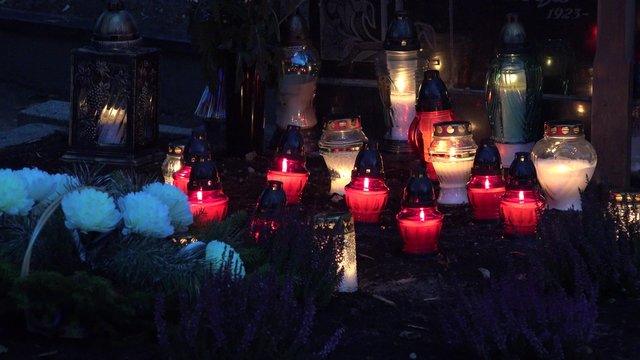 group of colorful candles burn on grave in graveyard. Static closeup shot.
