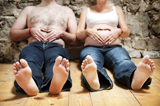 Close-up of a bellies with the mom's and dad's hands making a heart shape,