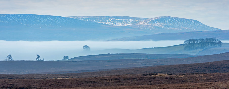 Scenic view over Melmerby Moor towards snow capped hills in Coverdale on a cool and misty early spring morning in the Yorkshire Dales National Park.