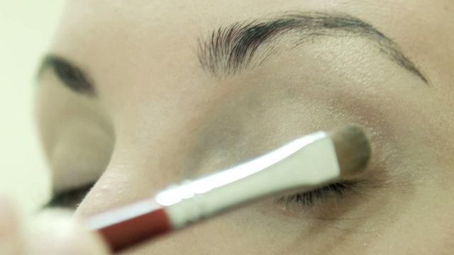 Professional makeup artist talking and applying makeup powder on a eyelid of client female, opposite mirror with light