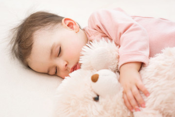 Close-up portrait of beautiful baby toddler girl sleeping with a fluffy teddy bear on the bed