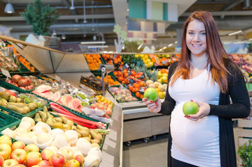 Pregnant woman with green apple choosing vegetables  in supermar