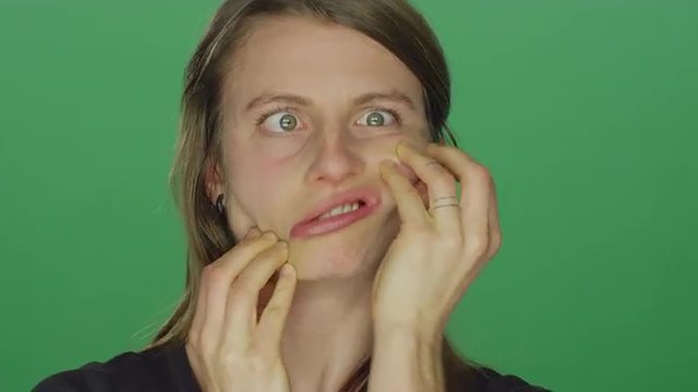Young woman makes funny faces and smiles, on a green screen studio background