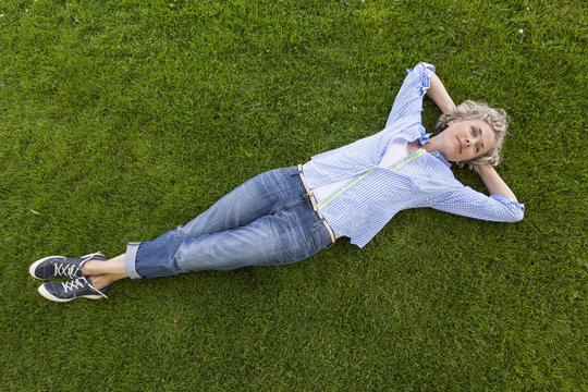 Middle-aged woman in casual weekend clothing relaxing on the grass in a park. She is smiling with a happy, contented expression and looks like she is daydreaming.
