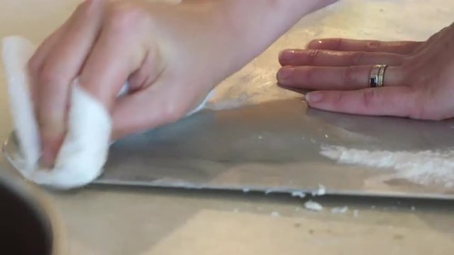 Detail of cook's hands scrubbing a baking tray with scouring powder and paper towels.  Shallow focus. Originally recorded in 4K, UHD.