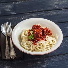 Spaghetti and meatballs in tomato sauce in a ceramic saucer on dark wooden background. Delicious food