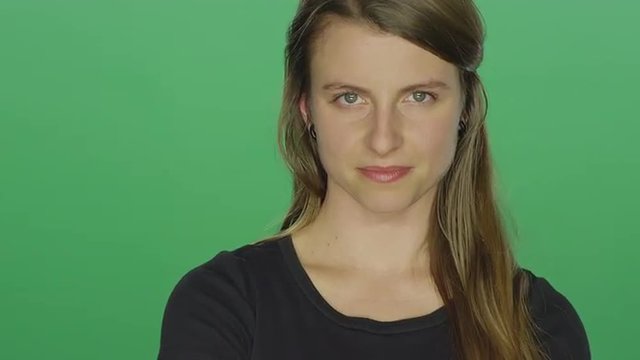 Young woman crosses her arms and glares, on a green screen studio background