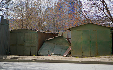 Fototapeta na wymiar Старые ржавые развалившиеся железные зеленые гаражи стоящие вдоль улицы