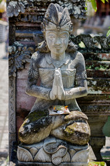 Stone sculpture of a praying woman with offering at a temple in Bali, Indonesia