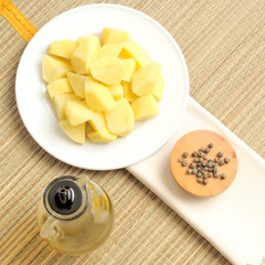 patate a cubetti su un piatto bianco, con olio e pepe, su una tovaglietta di bambu, vista dall'alto, luce naturale, quadrata