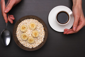 Woman hands holding spoon, healthy breakfast - eggs, black coffee and Oats flakes with banana. Whole grain cereal.