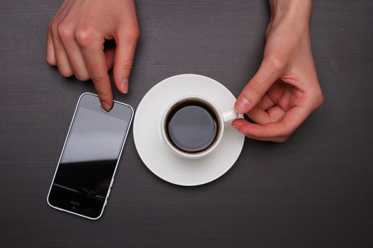 Woman Hands Touching Smart Phone And Holding Coffee Cup. Top View