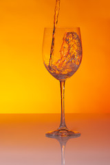 Falling water flow into a big wineglass and creating a human head silhouette on orange background.