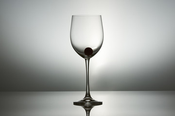 Big size wineglass with grape on bottom standing on a table on gray background.
