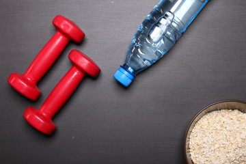 Oat flakes bottle of water and Red dumbbell table. fitness and healthy food concept.