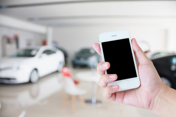 hands holding mobile phone with new cars in showroom